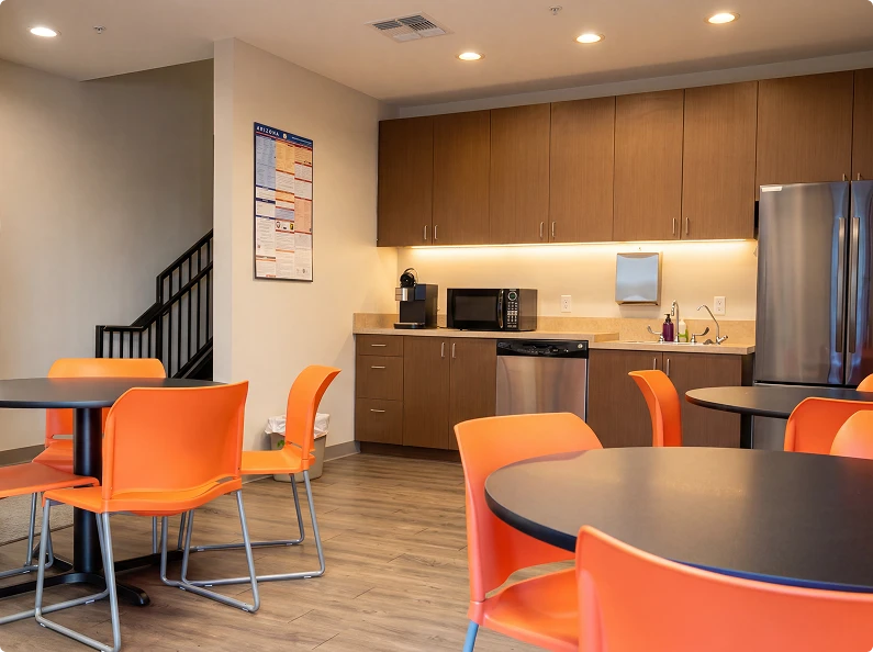 Community dining area with round tables, orange chairs, and kitchenette